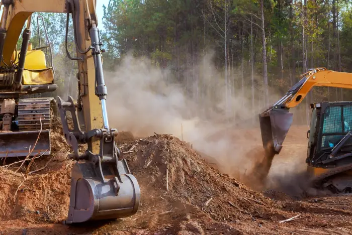 Excavator and skid steer loader working on a construction site, moving dirt and creating dust.