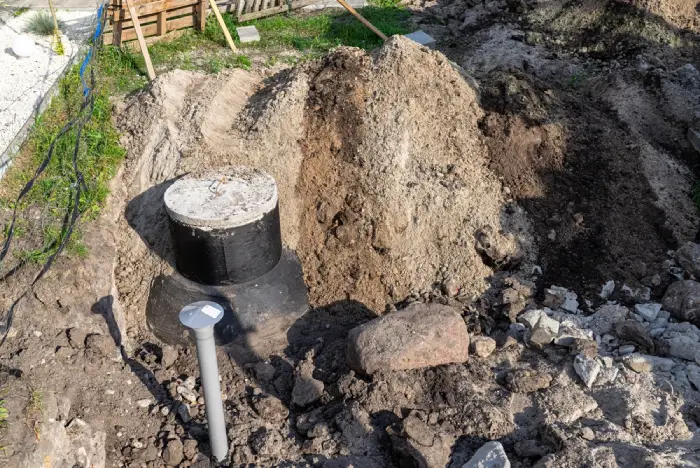 Construction site showing a newly installed black concrete septic tank or utility vault in a dirt trench.